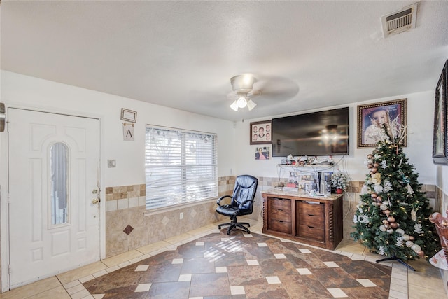 tiled entrance foyer featuring tile walls, ceiling fan, and a textured ceiling