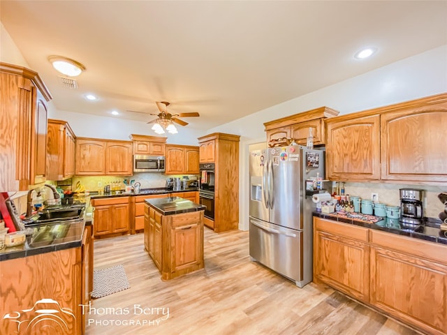 kitchen with appliances with stainless steel finishes, light wood-type flooring, ceiling fan, sink, and a center island