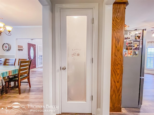 hall featuring crown molding, light hardwood / wood-style floors, and an inviting chandelier