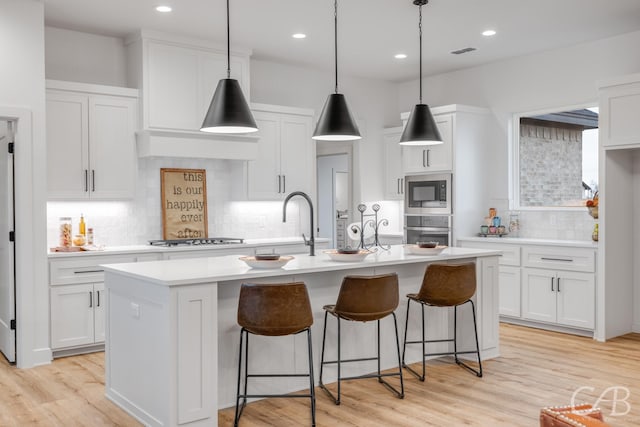 kitchen featuring white cabinets, appliances with stainless steel finishes, a center island with sink, and decorative backsplash