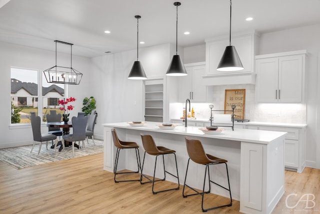 kitchen with decorative backsplash, light wood-type flooring, white cabinetry, and an island with sink