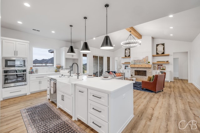 kitchen featuring appliances with stainless steel finishes, light wood-type flooring, a kitchen island with sink, white cabinetry, and hanging light fixtures