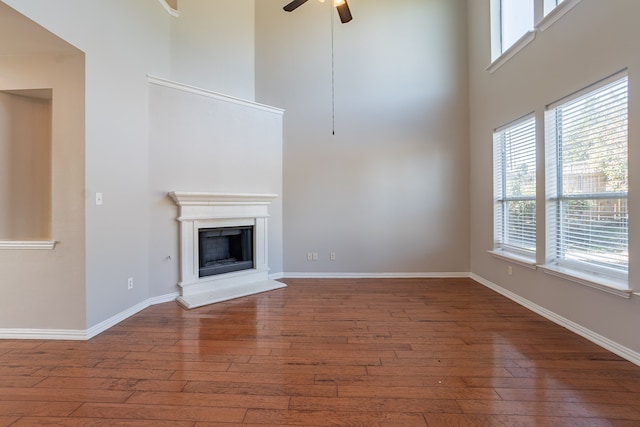 unfurnished living room featuring hardwood / wood-style flooring, ceiling fan, and a towering ceiling