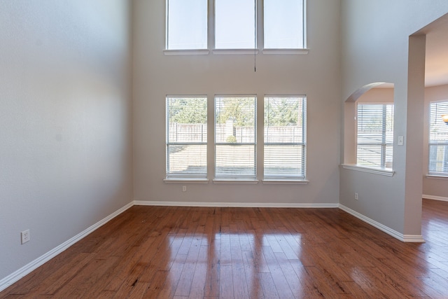 empty room with hardwood / wood-style floors and a towering ceiling