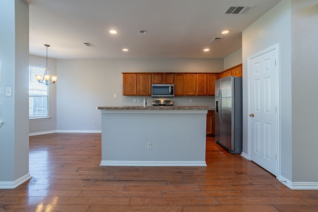 kitchen featuring appliances with stainless steel finishes, hanging light fixtures, a notable chandelier, a center island with sink, and dark hardwood / wood-style flooring