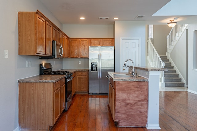 kitchen featuring appliances with stainless steel finishes, sink, a center island with sink, and dark wood-type flooring