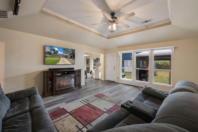 living room featuring ornamental molding, a raised ceiling, ceiling fan, a fireplace, and light hardwood / wood-style floors