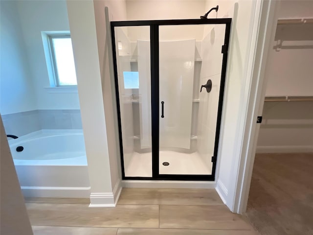 bathroom featuring a walk in closet, a bath, baseboards, and a stall shower