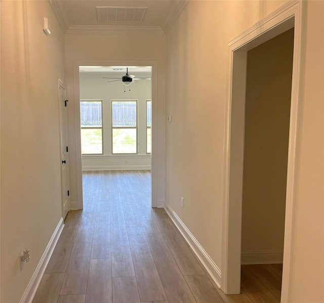 corridor with wood finished floors, visible vents, baseboards, and ornamental molding