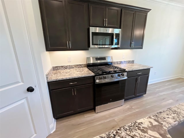 kitchen with light wood-style flooring, appliances with stainless steel finishes, baseboards, and light stone counters