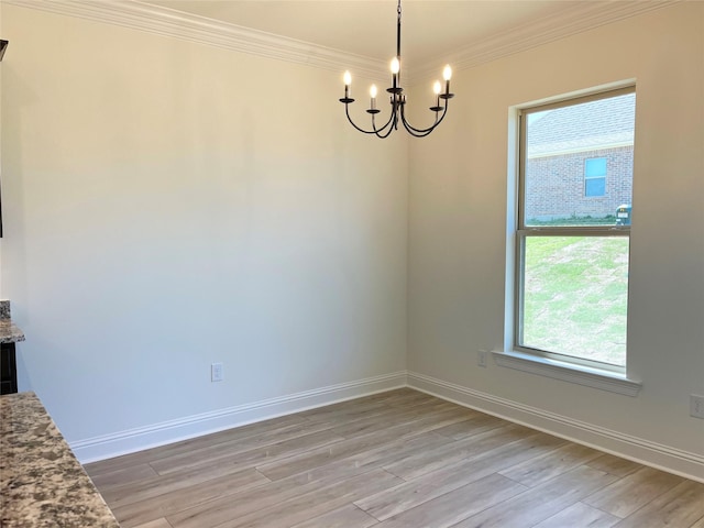 unfurnished dining area with an inviting chandelier, ornamental molding, light wood finished floors, and baseboards