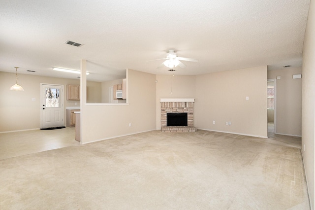 unfurnished living room featuring ceiling fan, light colored carpet, a brick fireplace, and a textured ceiling