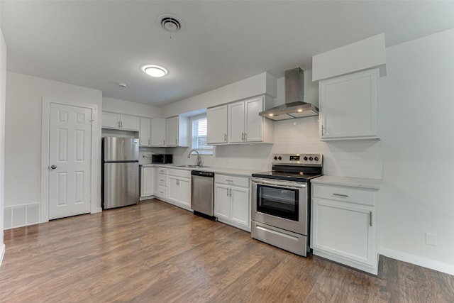 kitchen featuring white cabinets, wall chimney exhaust hood, dark hardwood / wood-style floors, decorative backsplash, and appliances with stainless steel finishes