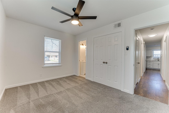 unfurnished bedroom with ensuite bath, ceiling fan, multiple windows, carpet floors, and a closet