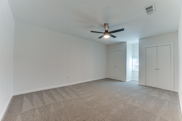 unfurnished bedroom with ceiling fan, light carpet, and multiple closets