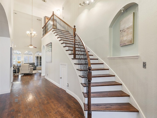 stairs featuring a towering ceiling, ceiling fan with notable chandelier, and hardwood / wood-style flooring