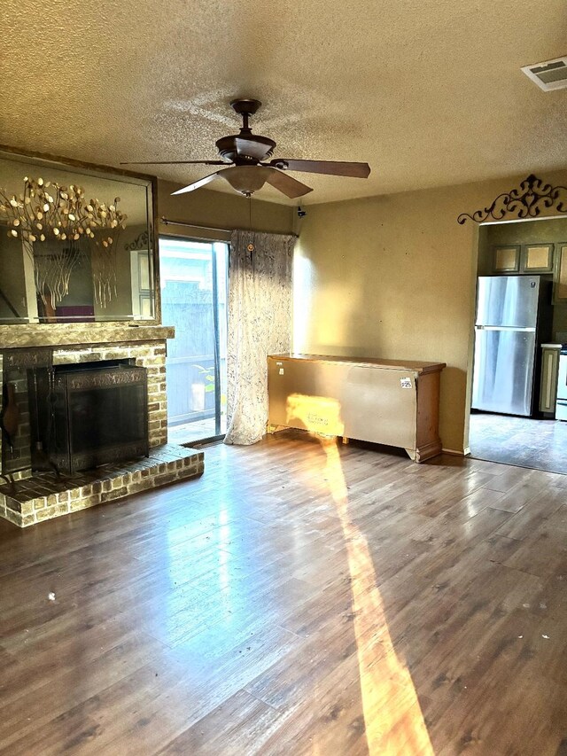 unfurnished living room featuring hardwood / wood-style floors, a textured ceiling, a brick fireplace, and ceiling fan