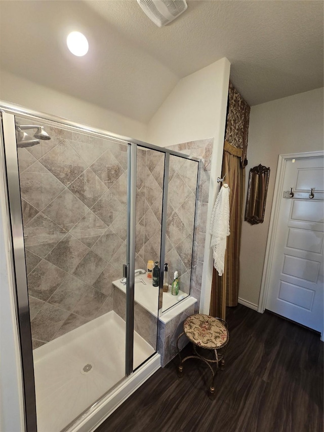 bathroom featuring a shower with door, vaulted ceiling, hardwood / wood-style flooring, and a textured ceiling