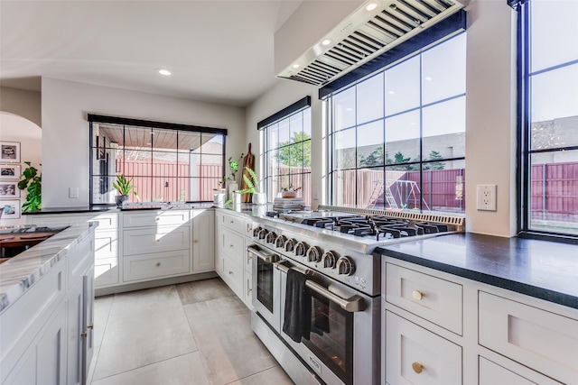 kitchen featuring premium range hood, range with two ovens, light tile patterned floors, arched walkways, and white cabinets