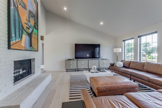 living room with light hardwood / wood-style flooring, vaulted ceiling, and a brick fireplace