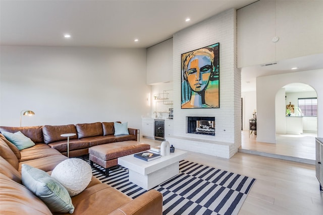 living room with a brick fireplace, beverage cooler, and light hardwood / wood-style flooring