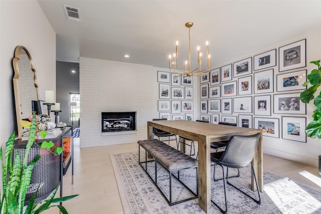 dining space featuring a fireplace, light hardwood / wood-style flooring, a notable chandelier, and brick wall