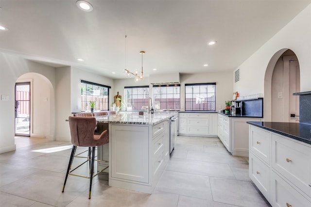 kitchen featuring white cabinetry, an island with sink, a chandelier, dark stone counters, and decorative light fixtures