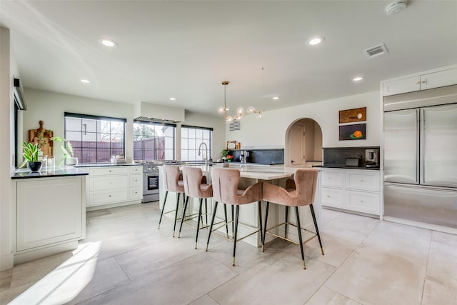 kitchen featuring hanging light fixtures, dark stone countertops, a center island with sink, white cabinets, and appliances with stainless steel finishes