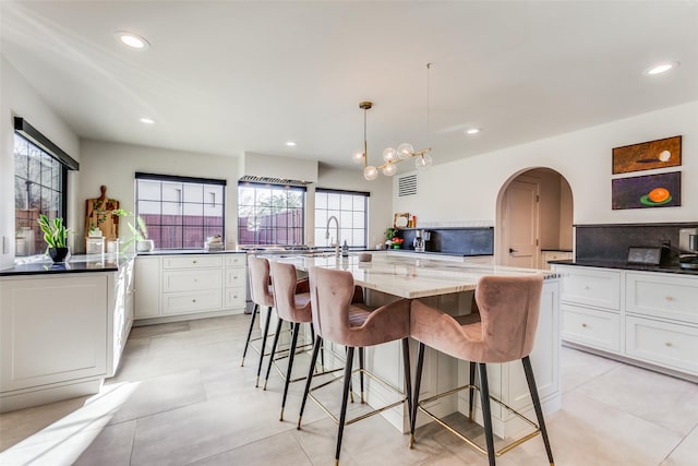 kitchen with a kitchen bar, light stone counters, a center island with sink, and pendant lighting