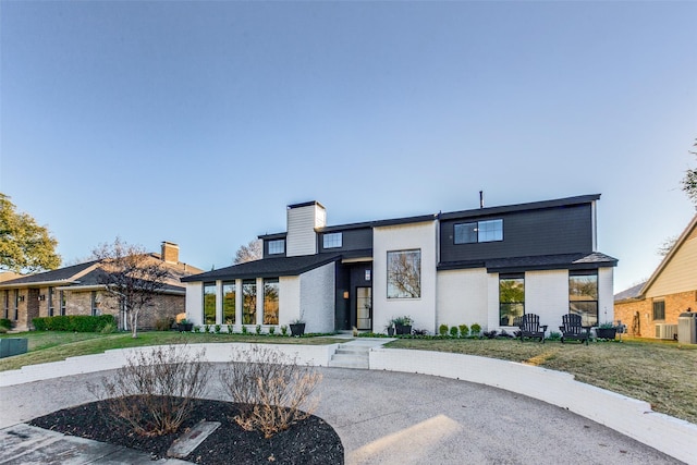 view of front of house featuring brick siding, central AC unit, a chimney, and a front yard