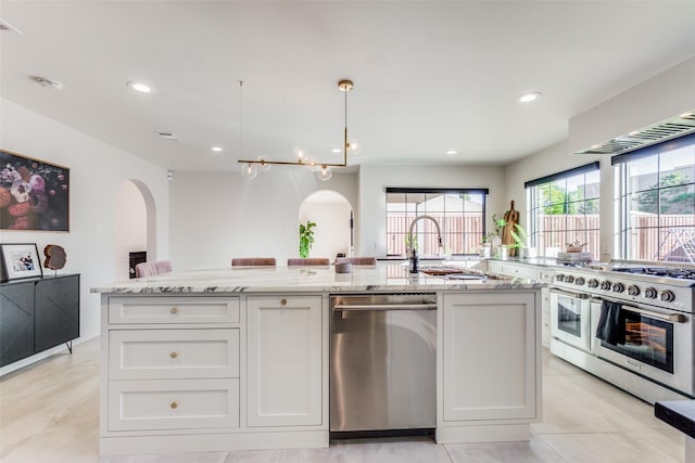 kitchen with white cabinets, decorative light fixtures, a center island with sink, light tile patterned floors, and appliances with stainless steel finishes