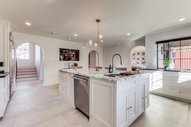 kitchen featuring a center island with sink, light stone countertops, appliances with stainless steel finishes, decorative light fixtures, and white cabinetry