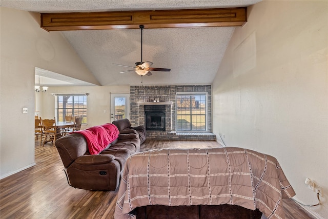 living room featuring vaulted ceiling with beams, a textured ceiling, a fireplace, ceiling fan with notable chandelier, and hardwood / wood-style flooring