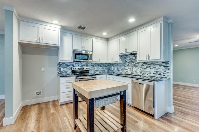 kitchen featuring tasteful backsplash, white cabinets, stainless steel appliances, and light wood-type flooring