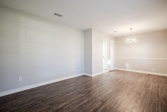 spare room with a chandelier and dark wood-type flooring