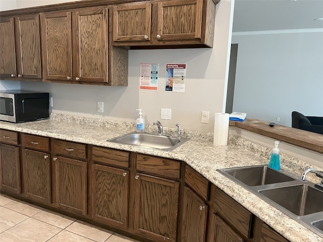 kitchen featuring crown molding, dark brown cabinets, sink, and light tile patterned floors