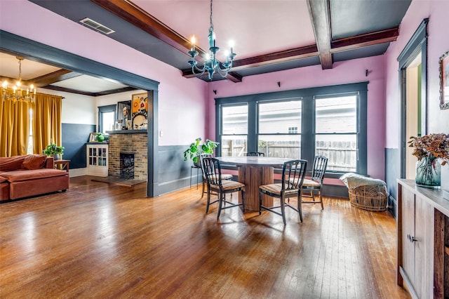 dining space featuring beamed ceiling, wood-type flooring, and an inviting chandelier