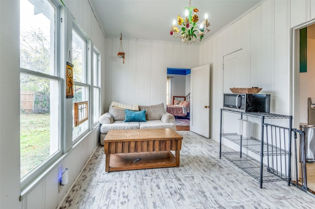 living area with light wood-type flooring, an inviting chandelier, wooden walls, and crown molding