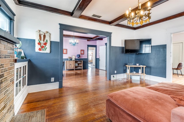 living room featuring beamed ceiling, hardwood / wood-style floors, a fireplace, and a notable chandelier