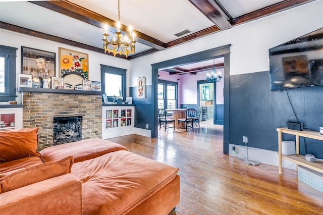 living room featuring a brick fireplace, beamed ceiling, wood-type flooring, and an inviting chandelier