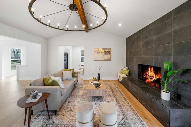 living room featuring a chandelier, light wood-type flooring, vaulted ceiling, and a tiled fireplace