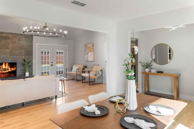 dining area featuring a tile fireplace, a notable chandelier, wood finished floors, visible vents, and french doors