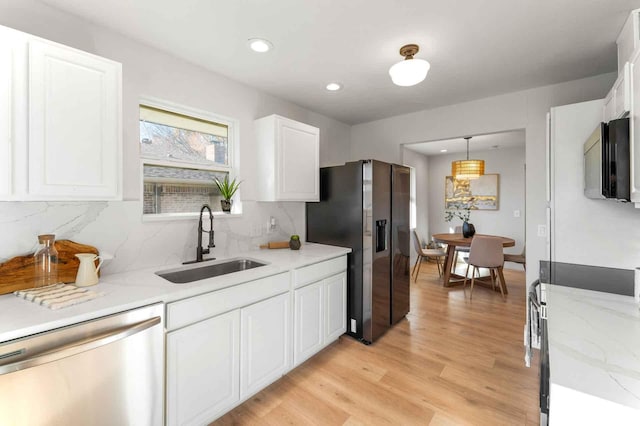 kitchen featuring stainless steel appliances, a sink, white cabinetry, light wood-style floors, and hanging light fixtures