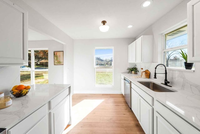 kitchen with light stone counters, light wood-style flooring, a sink, white cabinets, and dishwasher