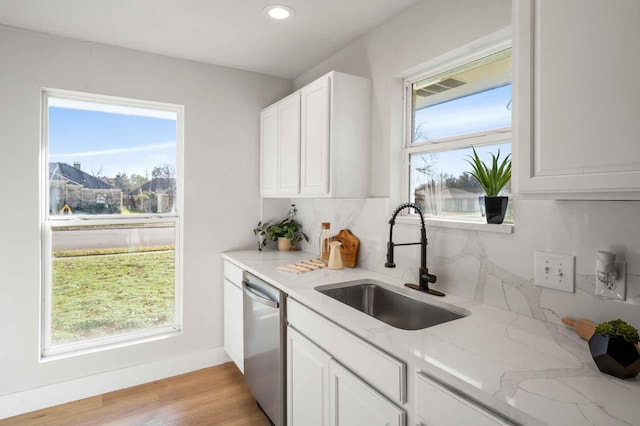 kitchen featuring light stone countertops, a healthy amount of sunlight, stainless steel dishwasher, white cabinetry, and a sink