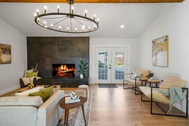 living room with french doors, vaulted ceiling, wood-type flooring, a notable chandelier, and a tiled fireplace