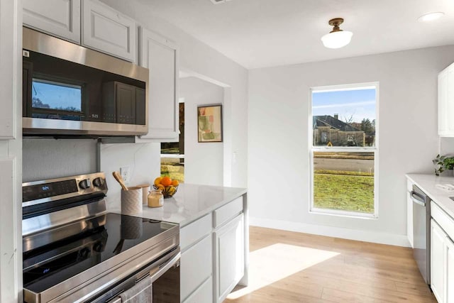 kitchen featuring baseboards, light stone countertops, stainless steel appliances, light wood-type flooring, and white cabinetry