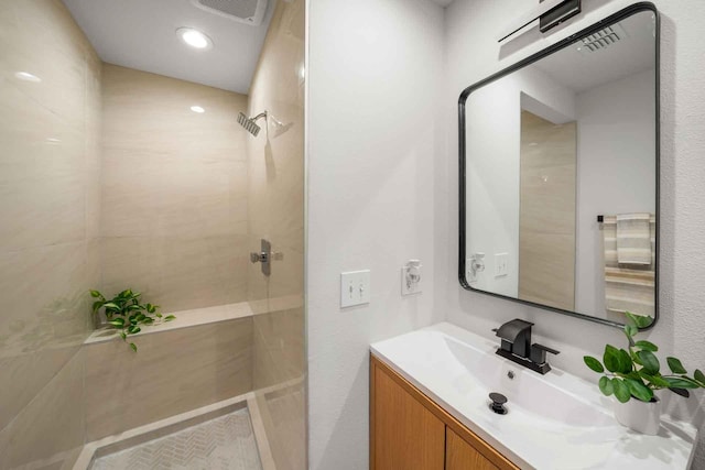 bathroom featuring visible vents, tiled shower, and vanity