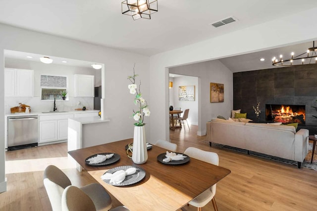 dining area featuring light wood-type flooring, a fireplace, visible vents, and lofted ceiling