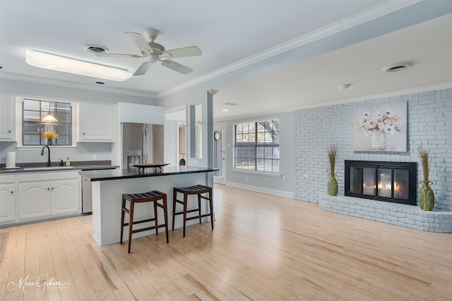 kitchen with a kitchen breakfast bar, stainless steel refrigerator with ice dispenser, a fireplace, ornamental molding, and white cabinets